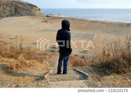Upset man standing in black jacket on destroyed stairs and looking at Japanese sea on an autumn day 118228178