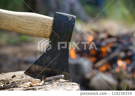 Close-up of an axe embedded in a log with a campfire burning in the background Close-up of an axe embedded in a log with a campfire burning in the background 118230359