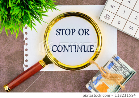 STOP OR CONTINUE written through a magnifying glass on a blank sheet, top view STOP OR CONTINUE written through a magnifying glass on a blank sheet, top view 118231554