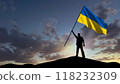 The silhouette of a man, standing on a small mountain, waves the Ukrainian flag, in the background a cloudy sky at dawn 118232309
