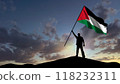 The silhouette of a man, standing on a small mountain, waves the Palestinian flag, in the background a cloudy sky at dawn 118232311