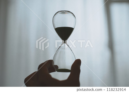 Silhouette of a person holding a glass hourglass Silhouette of a person holding a glass hourglass 118232914