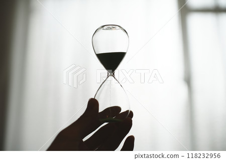 Silhouette of a person holding a glass hourglass Silhouette of a person holding a glass hourglass 118232956