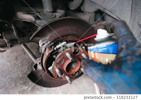 A mechanic cleans a dust the inside of a car brake drum with cleaning spray 118233127