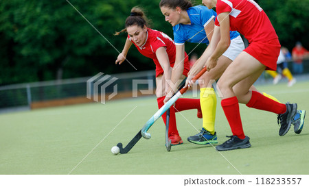 Three female players compete for the ball during a field hockey match 118233557