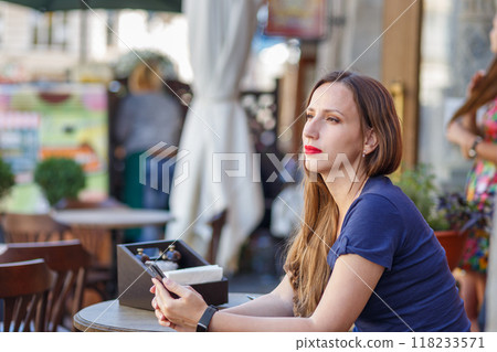 A woman enjoys a sunny day at an outdoor cafe in a vibrant city A woman enjoys a sunny day at an outdoor cafe in a vibrant city 118233571