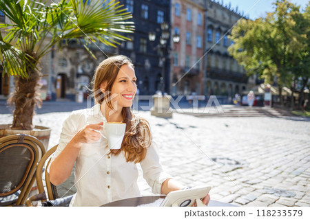 Young woman enjoying coffee at a charming cafe in the heart of a historic town square Young woman enjoying coffee at a charming cafe in the heart of a historic town square 118233579