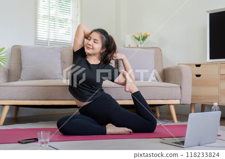 Woman practicing yoga pose with laptop guidance at home Woman practicing yoga pose with laptop guidance at home 118233824