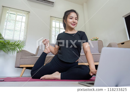 Woman practicing yoga with laptop in cozy home setting Woman practicing yoga with laptop in cozy home setting 118233825