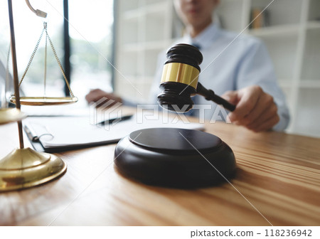 Lawyer Holding Gavel with Scales of Justice on Desk 118236942