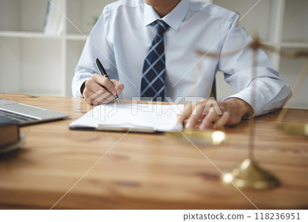 A lawyer in a suit is sitting at his desk, signing legal documents with a gavel on the side. 118236951