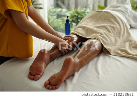 Massagist Treating Client's Leg in Spa Setting 118238681