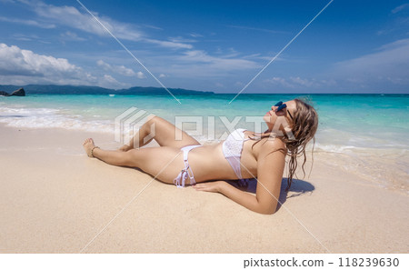 A woman relaxes on a sandy beach under a clear blue sky while enjoying the sun and ocean waves during a summer day 118239630