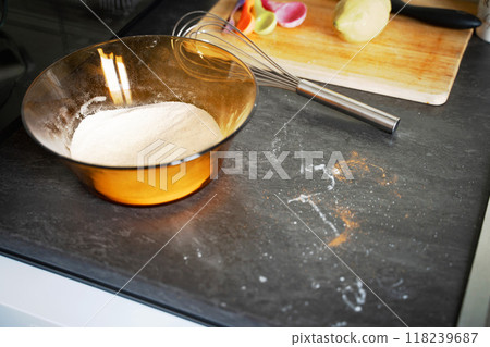 On the kitchen counter, a bowl filled with flour sits prominently beside a whisk, ready for various baking and cooking tasks On the kitchen counter, a bowl filled with flour sits prominently beside a whisk, ready for various baking and cooking tasks 118239687