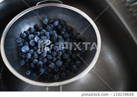 A large strainer filled to the brim with fresh blueberries sits in a clean, shiny sink, ready for washing and preparation 118239688
