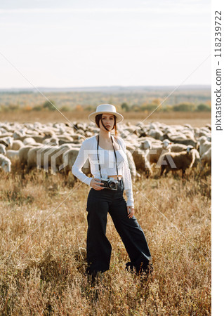 Young woman with a camera in front of a herd of sheep. Nature, fashion, vacation and lifestyle. 118239722