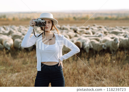 Young woman with a camera in front of a herd of sheep. Nature, fashion, vacation and lifestyle. 118239723