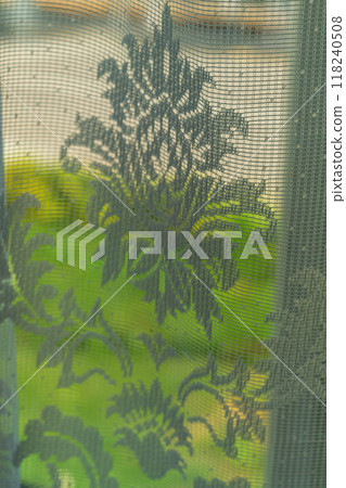 Blurry vertical photo of transparent thin window curtain against green vegetation background and trees outside window. Blank for the background in artworks. Blurry vertical photo of transparent thin window curtain against green vegetation background and trees outside window. Blank for the background in artworks. 118240508