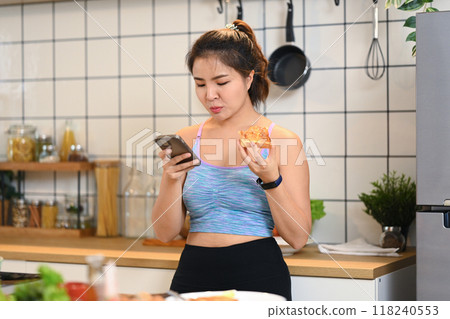 Young asian woman eating toasted bread for breakfast and using mobile phone in kitchen 118240553