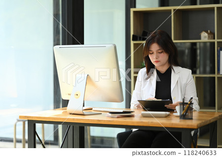 Concentrated young businesswoman analyzing statistics data documents at office desk Concentrated young businesswoman analyzing statistics data documents at office desk 118240633