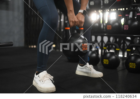 Unrecognizable female athlete strength training legs, lifting a kettlebell in a gym. Healthy lifestyle Unrecognizable female athlete strength training legs, lifting a kettlebell in a gym. Healthy lifestyle 118240634