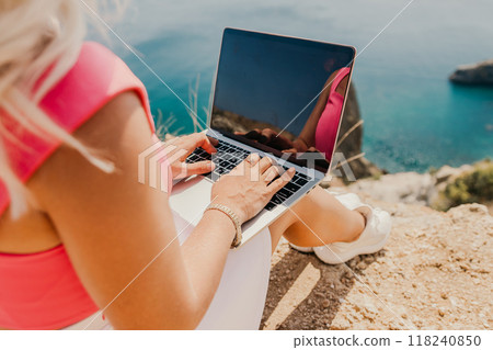 A woman is sitting on a rock by the ocean, typing on her laptop. Concept of relaxation and leisure, as the woman enjoys the beautiful view of the water while working on her computer. A woman is sitting on a rock by the ocean, typing on her laptop. Concept of relaxation and leisure, as the woman enjoys the beautiful view of the water while working on her computer. 118240850