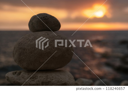 Stones Stacked Sunset Beach - A balanced stack of rocks stands on a beach with a fiery sunset in the background. Stones Stacked Sunset Beach - A balanced stack of rocks stands on a beach with a fiery sunset in the background. 118240857