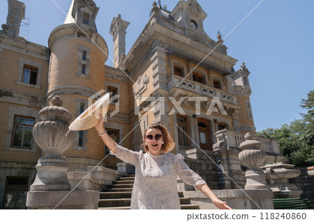 A woman is standing in front of a large building, holding a straw hat A woman is standing in front of a large building, holding a straw hat 118240860
