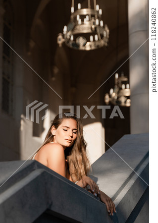 Woman Chandelier Staircase - A woman leans against a staircase in a building with ornate chandeliers hanging overhead. Woman Chandelier Staircase - A woman leans against a staircase in a building with ornate chandeliers hanging overhead. 118240862