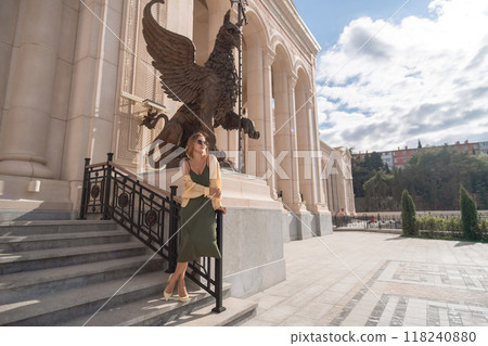 Woman, Sculpture, Building - A woman stands on steps in front of a sculpture of a griffin at an ornate building. Woman, Sculpture, Building - A woman stands on steps in front of a sculpture of a griffin at an ornate building. 118240880