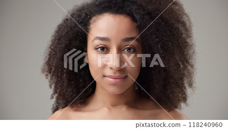 Beauty and healthcare - beautiful African American woman with curly afro hairstyle and clean, healthy skin, standing on a gray studio background opening and closing her eyes looking at the camera 118240960