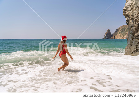 A woman in Santa hat on the seashore, dressed in a red swimsuit. New Year's celebration in a hot country. 118240969