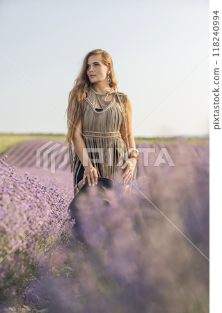 A woman is standing in a field of purple flowers, wearing a black dress and a black hat. 118240994