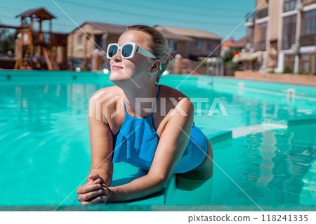 Bikini-clad woman enjoys poolside relaxation. Poolside ambiance. Capturing woman's relaxed time near pool. 118241335