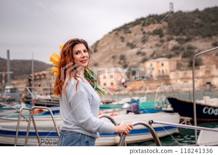 Woman holds yellow tulips in harbor with boats docked in the background., overcast day, yellow sweater, mountains Woman holds yellow tulips in harbor with boats docked in the background., overcast day, yellow sweater, mountains 118241336