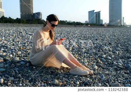 Woman browsing smartphone sitting on pebble coast in Batumi city Georgia. Woman browsing smartphone sitting on pebble coast in Batumi city Georgia. 118242388