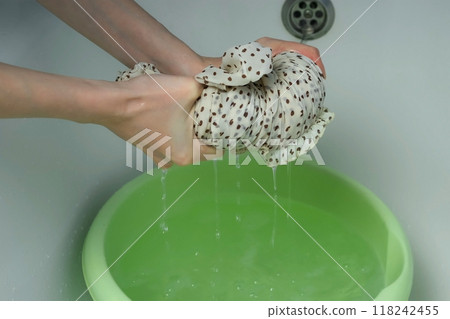 A woman wrings out a hand-washed dress over a basin, closeup view. 118242455
