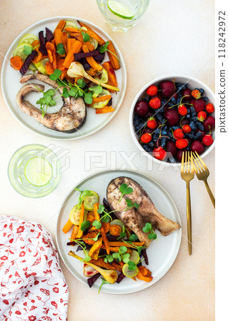 Baked silver carp with roasted carrots, zucchini, beets, and garlic, accompanied by fresh seasonal fruits like cherries, strawberries, and honeysuckle 118242972