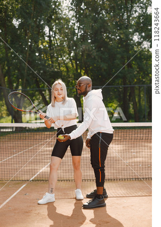 Coach and tennis player. Black race man giving lesson to a woman. Outside court setting. 118243664