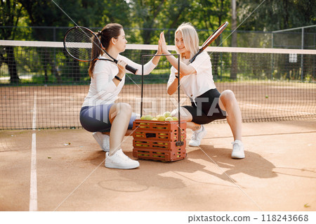 Female friends with racquets and box of balls on the tennis court. Summer, outside court. Female friends with racquets and box of balls on the tennis court. Summer, outside court. 118243668