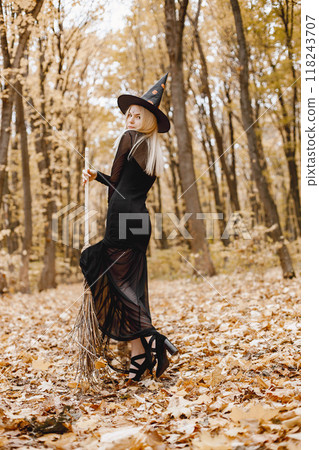 Blonde young girl witch in forest on Halloween. Girl wearing black dress and cone hat. Witch holding a broom. 118243707