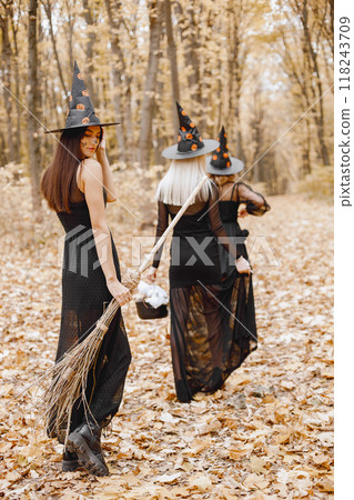 Three girls witches in forest on Halloween. Girls wearing black dresses and cone hats. Witches holding a magician stuff. Three girls witches in forest on Halloween. Girls wearing black dresses and cone hats. Witches holding a magician stuff. 118243709