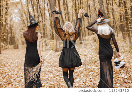 Three girls witches in forest on Halloween. Girls wearing black dresses and cone hats. Witches holding a magician stuff. Three girls witches in forest on Halloween. Girls wearing black dresses and cone hats. Witches holding a magician stuff. 118243710