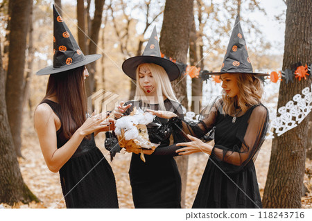 Three young girls witches in forest on Halloween. Girls wearing black dresses and cone hat. Witches holding a magician cauldron. 118243716