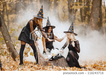 Three girls witches in forest on Halloween. Girls wearing black dresses and cone hats. Witches make a magic potion. Three girls witches in forest on Halloween. Girls wearing black dresses and cone hats. Witches make a magic potion. 118243718