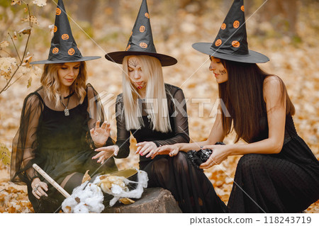 Three girls witches in forest on Halloween. Girls wearing black dresses and cone hats. Witches make a magic potion. 118243719