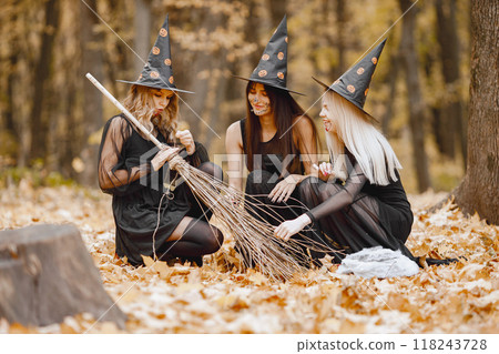 Three young girls witches in forest on Halloween. Girls wearing in black dresses and cone hat. Witch holding a broom. Three young girls witches in forest on Halloween. Girls wearing in black dresses and cone hat. Witch holding a broom. 118243728
