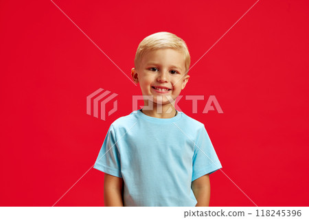 Portrait of little 4 years old boy with blonde hair, standing with cheerful smile, wearing blue t-shirt and posing against red studio background Portrait of little 4 years old boy with blonde hair, standing with cheerful smile, wearing blue t-shirt and posing against red studio background 118245396