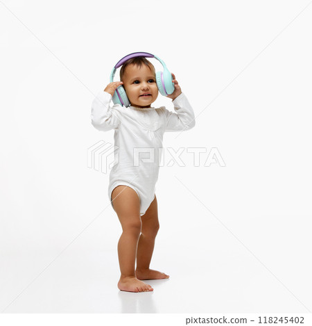 Happy little baby girl, child standing in onesie listening to music, fairy tales on headphones isolated on white studio background Happy little baby girl, child standing in onesie listening to music, fairy tales on headphones isolated on white studio background 118245402