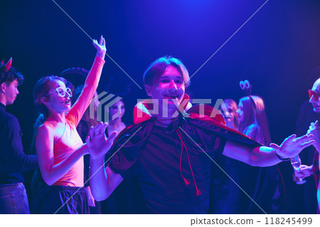 Group of young friends in Halloween costumes sharing laugh at party at nightclub, cheerfully dancing and having fun. 118245499
